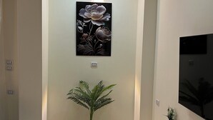 Un couloir moderne agrémenté d’une grande plante en pot, d’une œuvre d’art accrochée au mur et d’un téléviseur à écran plat posé sur une console noire.