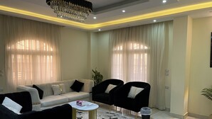 Un salon moderne avec un canapé beige, des fauteuils noirs, une petite table ronde et un lustre.