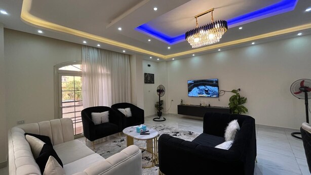 Un salon moderne avec un canapé beige, des fauteuils noirs, une table basse ronde et un lustre.