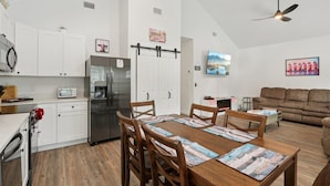 Una cocina moderna con armarios blancos, un refrigerador de acero inoxidable y un comedor con mesa y sillas de madera.