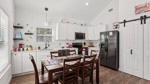 Una cocina moderna con armarios blancos, un refrigerador de acero inoxidable y una mesa de comedor con sillas.