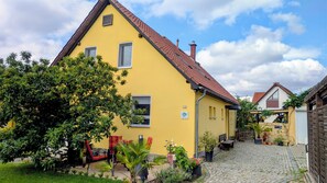 A yellow building with a red roof, a paved courtyard, and potted plants.