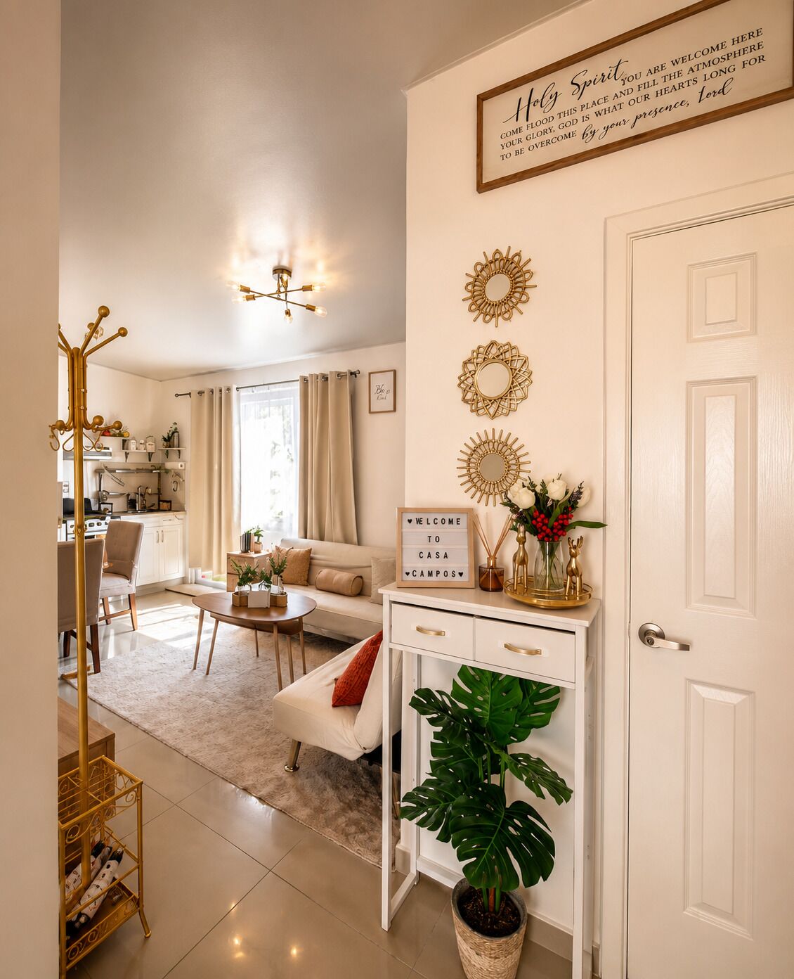 Una sala moderna con un sofá, una mesa de centro y un espejo decorativo. Hay una puerta blanca con un cartel arriba y una planta en el suelo.