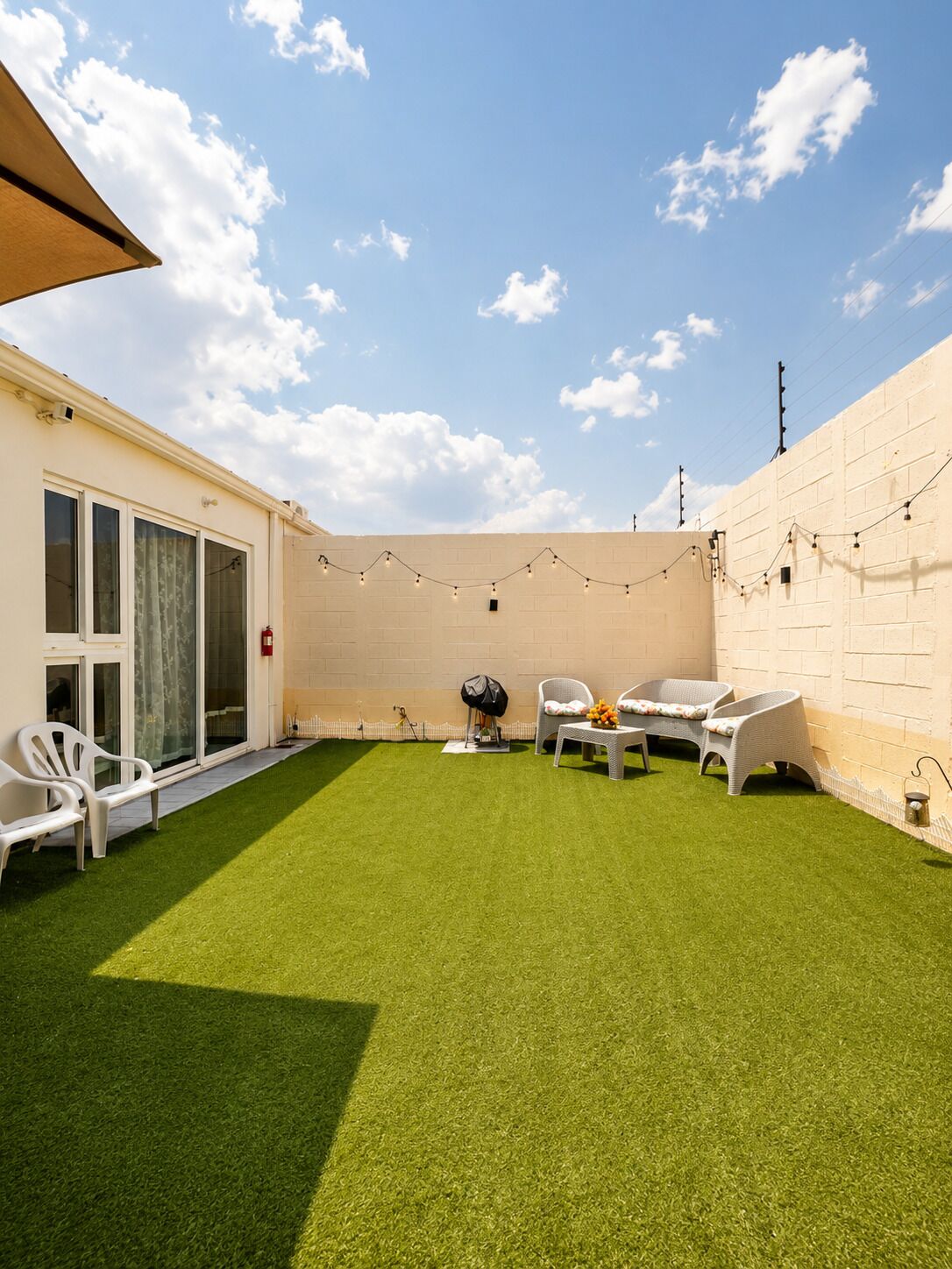 A backyard with artificial grass, white chairs, a table, and string lights.