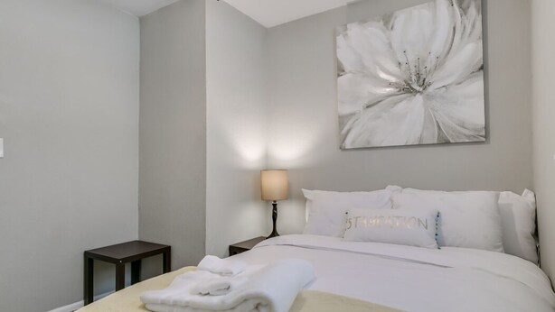 A neatly arranged hotel room with a bed, a bedside lamp, a small table, and a large floral artwork on the wall. - Melbourne 6 bed/2 bath Sleeps 12 BEDS 3King/3Qn/2twin (Melbourne)