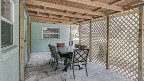 An outdoor patio with a wooden table and chairs, a lattice fence, and a window with blinds. - Melbourne 6 bed/2 bath Sleeps 12 BEDS 3King/3Qn/2twin (Melbourne)