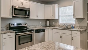 A kitchen with white cabinets, a stainless steel microwave, a stove, and a dishwasher. - Melbourne 6 bed/2 bath Sleeps 12 BEDS 3King/3Qn/2twin (Melbourne)