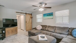 A living room with a large flat-screen TV, a ceiling fan, a sliding door, a sofa, and a painting on the wall. - Melbourne 6 bed/2 bath Sleeps 12 BEDS 3King/3Qn/2twin (Melbourne)