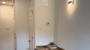 Een kleine kamer met een houten bureau, een zwarte stoel en een witte kledingkast.