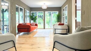 A spacious living room with a wooden floor, two sofas, and a large window offering a view of greenery.