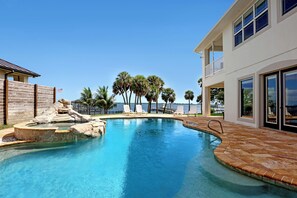 A swimming pool with a rock feature, lounge chairs, and a view of the ocean.
