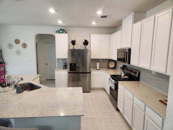 A modern kitchen with white cabinets, stainless steel appliances, and a marble countertop.