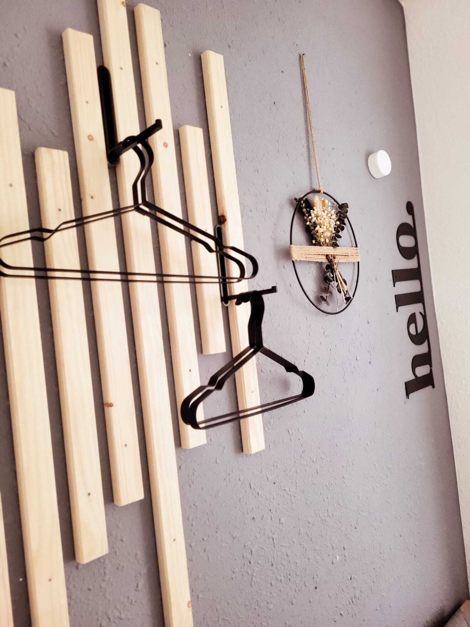 A wall with wooden planks, black hangers, and a decorative item with a string and flowers.