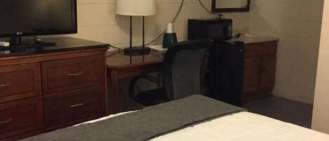 Una habitación de hotel con una cama, un escritorio con computadora, televisor y espejo.