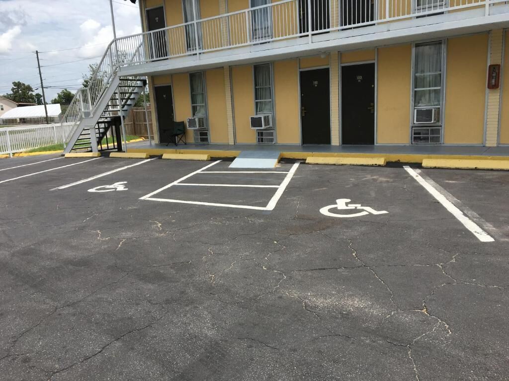 Un bâtiment à la façade jaune, doté d’une place de stationnement accessible aux personnes à mobilité réduite et d’un escalier menant à un balcon.