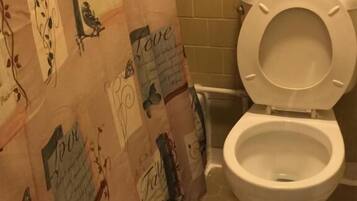 A bathroom with a toilet, a shower curtain with 'Hope' and 'Love' text, and a tiled floor.