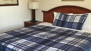 Una cama bien tendida con colcha azul y blanca a cuadros, cabecera de madera y mesita de noche con lámpara.