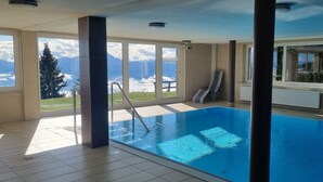 Piscina interior con vistas a montañas a través de grandes ventanales.