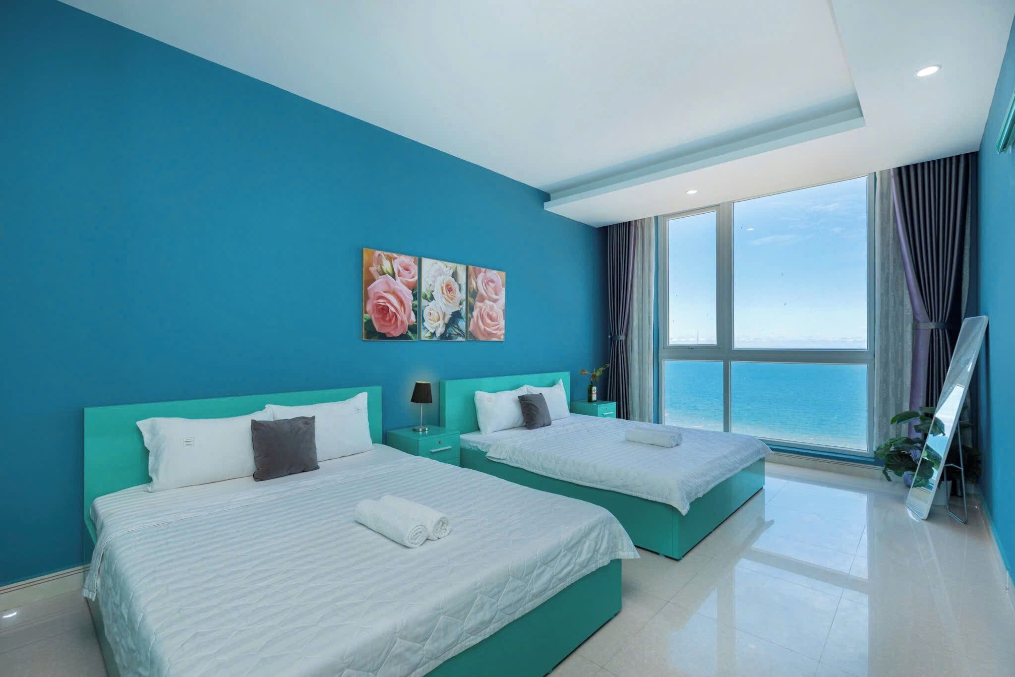 A modern hotel room with two beds, a large window with a view, and a teal color scheme.