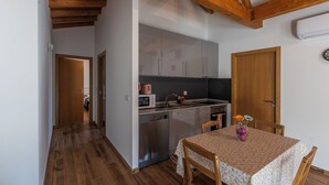 A compact kitchen with wooden beams, a dishwasher, and a dining table with a floral tablecloth. - Outeiro 7 (Penacova)