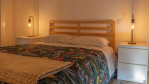 A neatly made bed with a colorful floral bedspread, two bedside tables with lamps, and a white nightstand. - Outeiro 7 (Penacova)