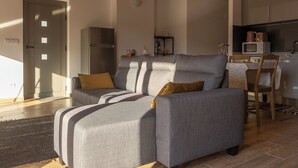 A modern living room with a grey sofa, a wooden dining table, and a kitchen area. - Outeiro 7 (Penacova)