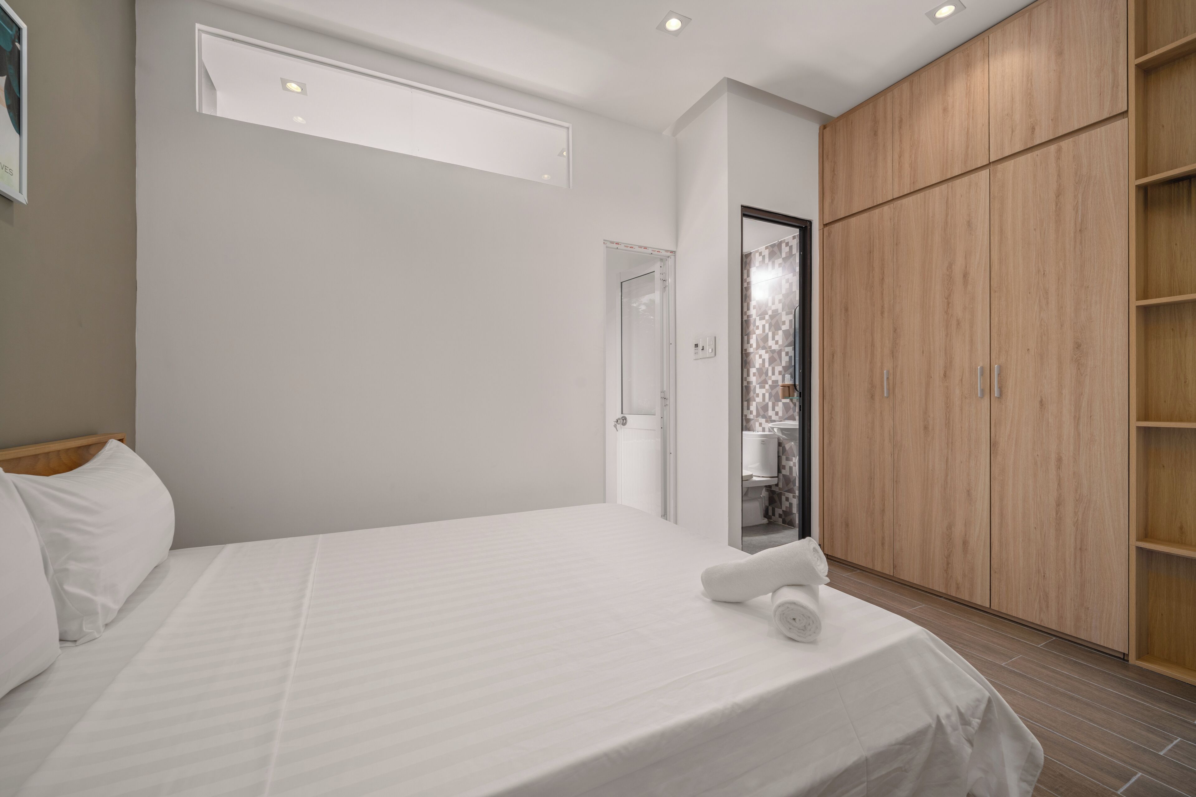 A modern bedroom with a large bed, wooden wardrobe, and a bathroom visible through an open door.