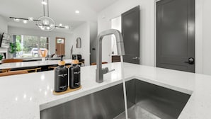 A modern kitchen with a stainless steel sink, a built-in oven, and a large island with a coffee machine and hand soap bottles. - Modern Luxury in West Midtown 4BR with Rooftop (Atlanta)