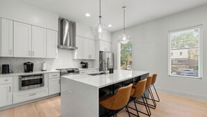 A modern kitchen with white cabinetry, stainless steel appliances, a central island with bar stools, and pendant lighting. - Modern Luxury in West Midtown 4BR with Rooftop (Atlanta)