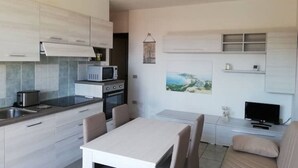 A modern kitchen with a dining area, a TV, and a small seating space. - House Relax sea view Sardinia (Funtana Meiga)