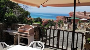 A patio with a grill, white chairs, and a view of the sea. - House Relax sea view Sardinia (Funtana Meiga)