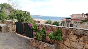 A stone wall with a garden bed, a stone pathway, and a view of the sea. - House Relax sea view Sardinia (Funtana Meiga)