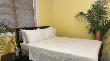 A bed with white bedding, a black nightstand with drawers, and a potted plant beside the bed.