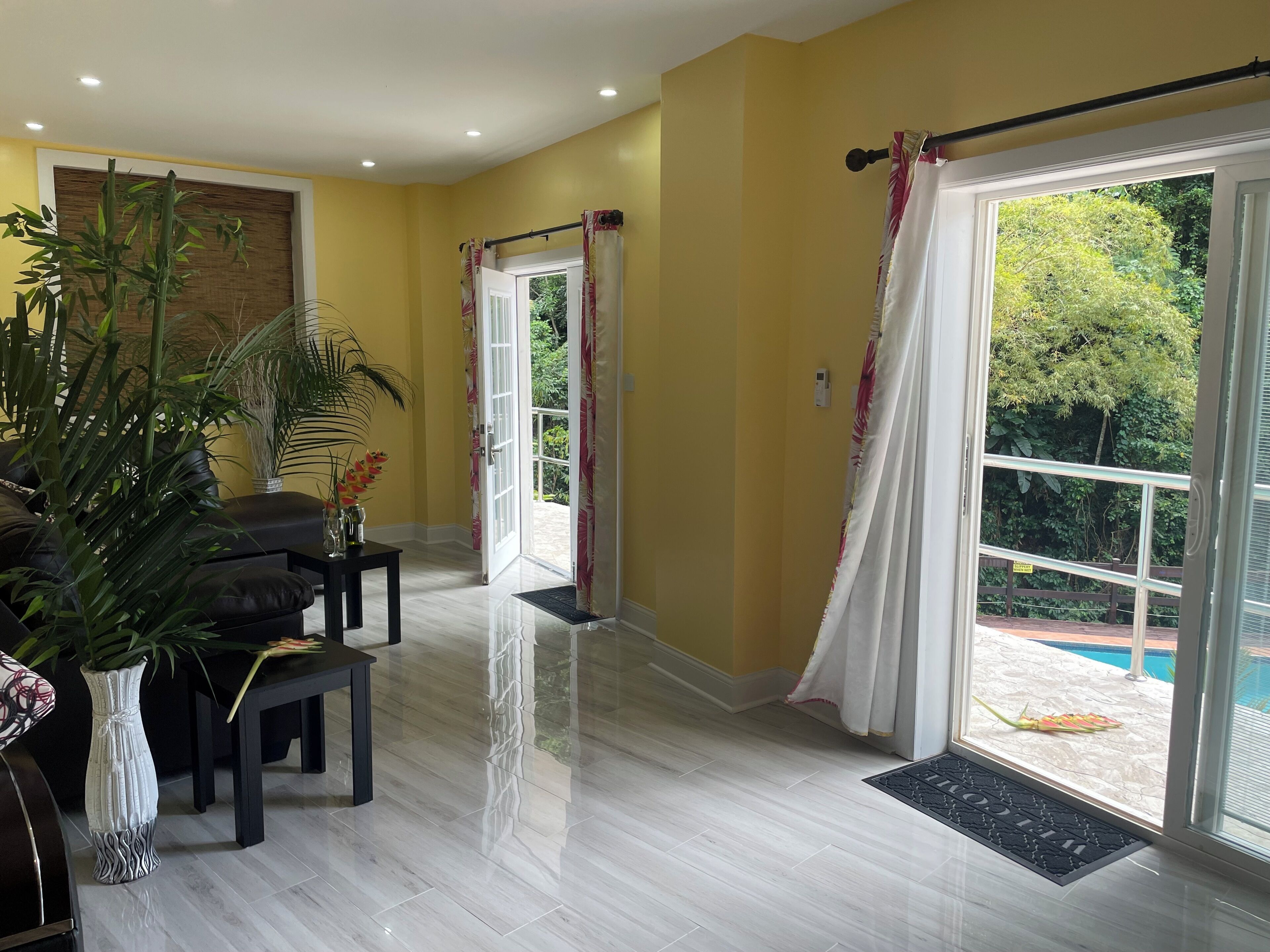 Un salón amplio con un gran ventanal, un sofá negro, una mesa de centro y una planta en maceta.