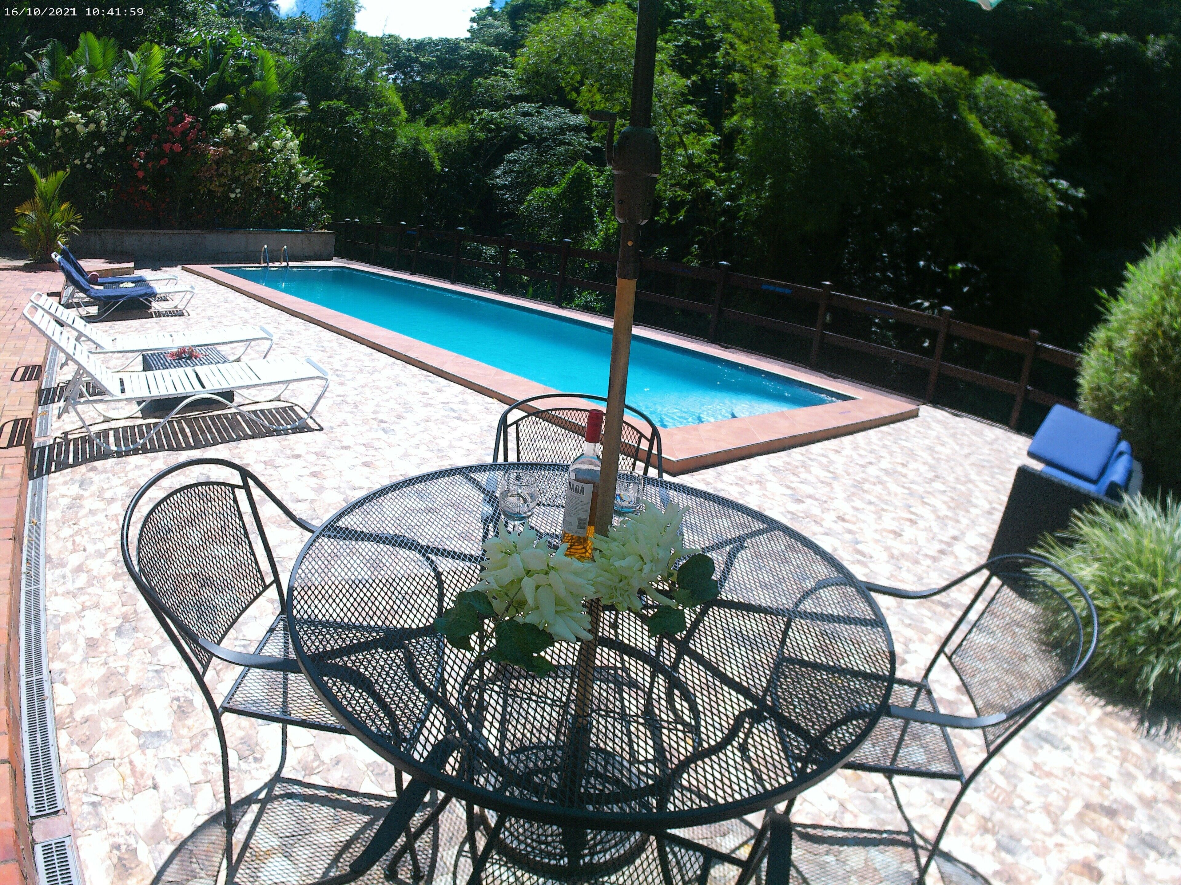 A poolside area with a table set for two, surrounded by lounge chairs and a pool.