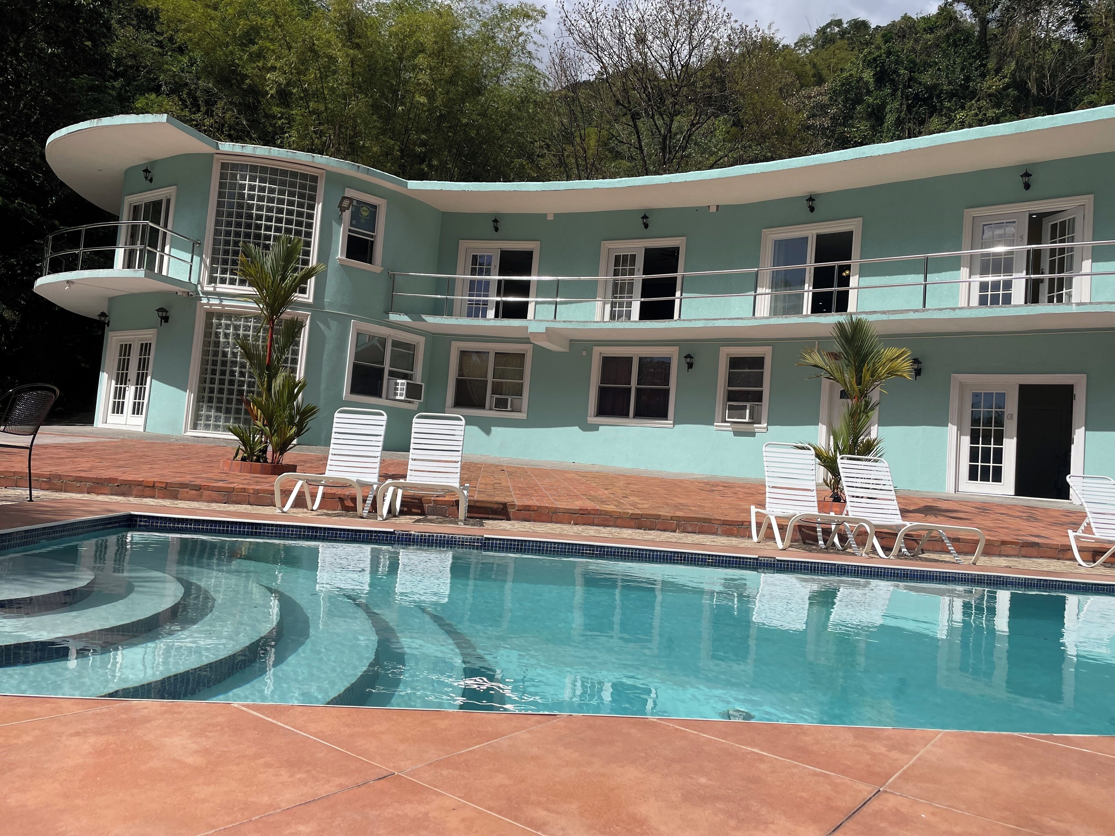 Un bâtiment à deux étages doté d’une piscine, de balustrades blanches et d’une terrasse carrelée.