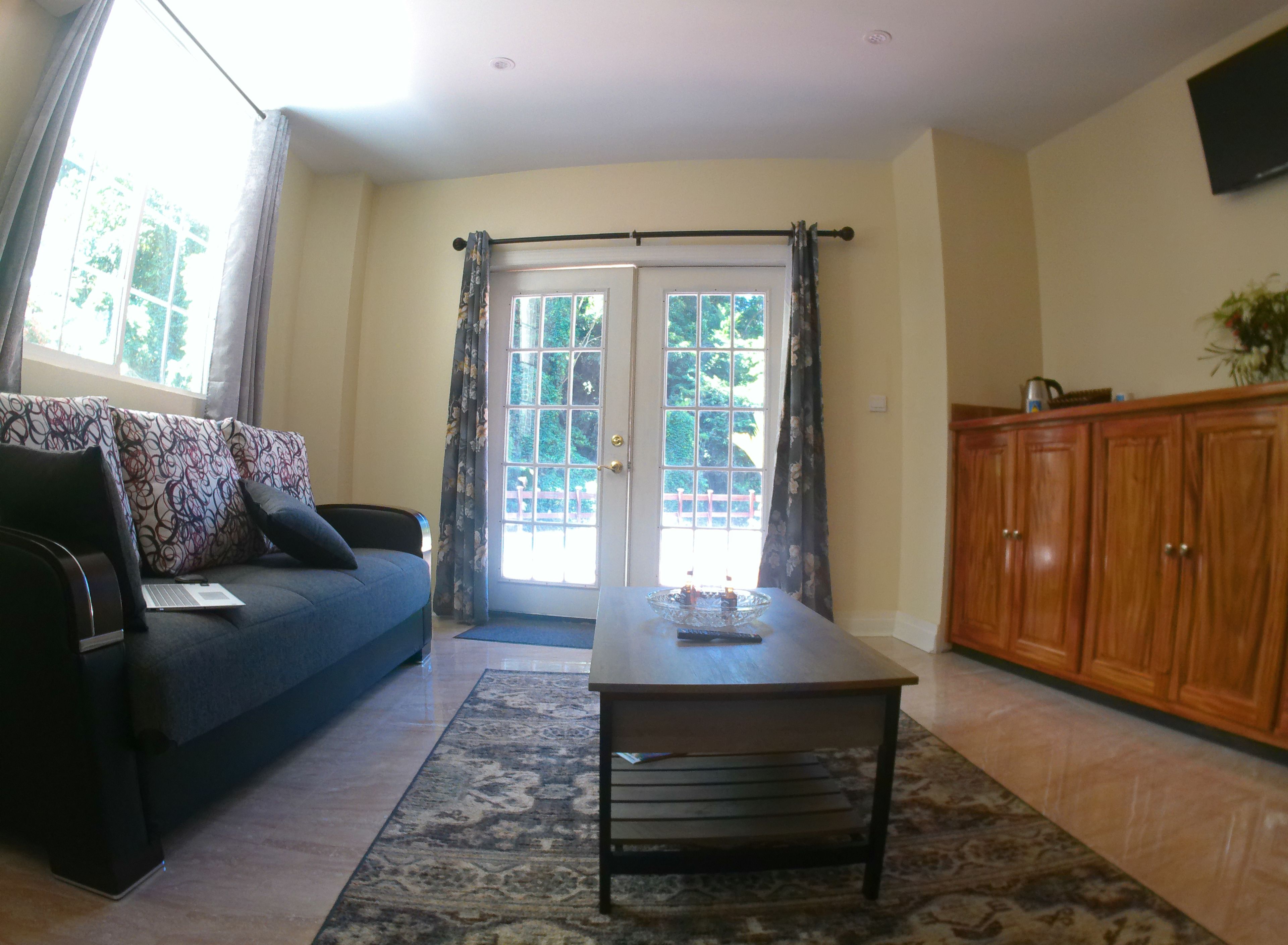A living room with a sofa, a coffee table, a wooden cabinet, and a door leading outside.