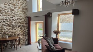 Un salon moderne avec un mur en pierre, une table à manger en bois avec des chaises, un canapé et une grande fenêtre donnant sur la rue.