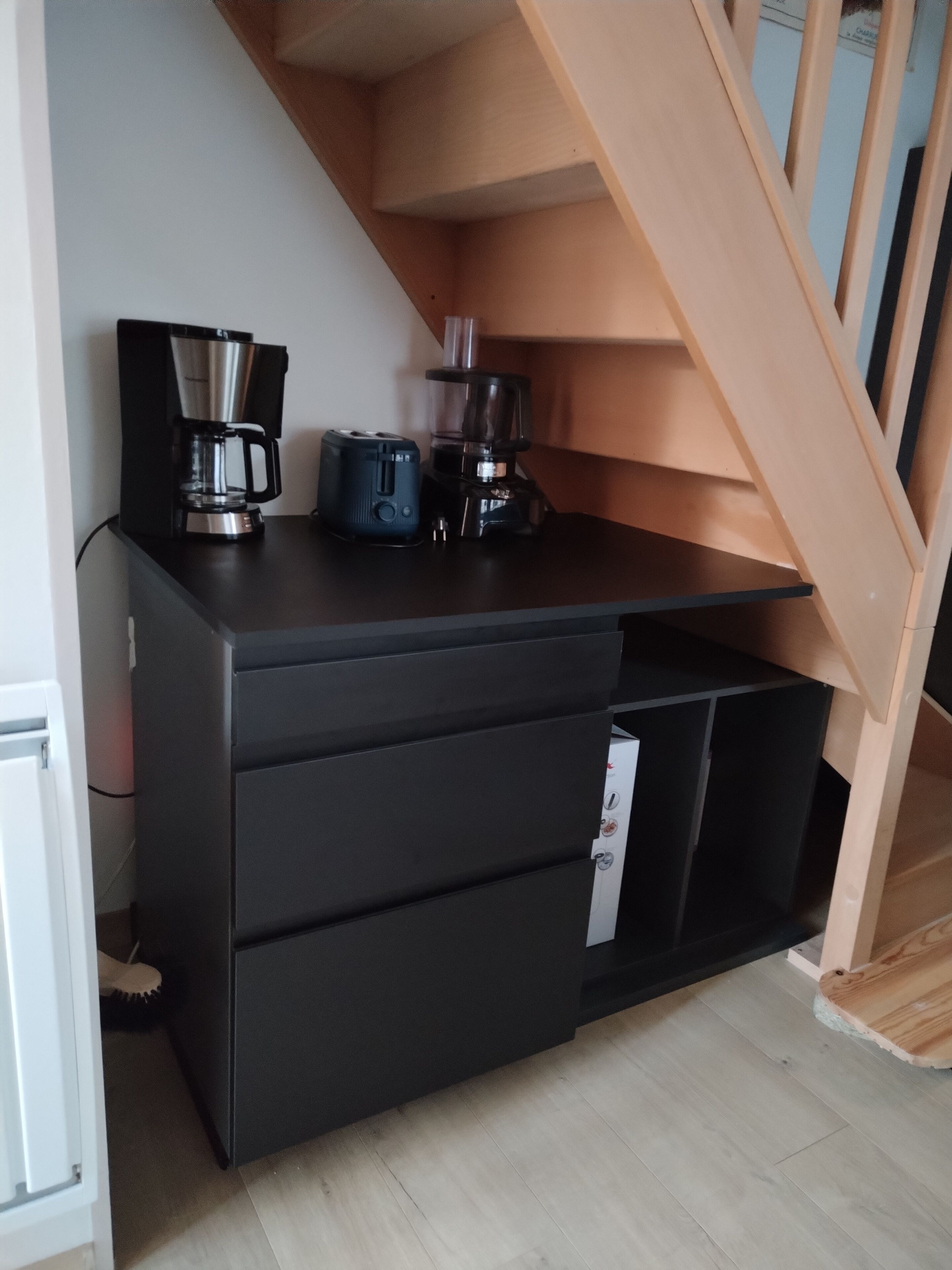 A kitchen area with a black countertop, a coffee maker, a blender, and a wooden staircase.