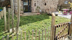 Un bâtiment en pierre avec une clôture en bois, un petit jardin et des sièges à l’extérieur.