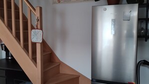 Une cuisine équipée d’un réfrigérateur en acier inoxydable, d’un escalier en bois et d’une plante fixée au mur.