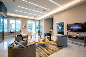 Um saguão de hotel moderno com uma televisão grande, assentos confortáveis e vista para o exterior.