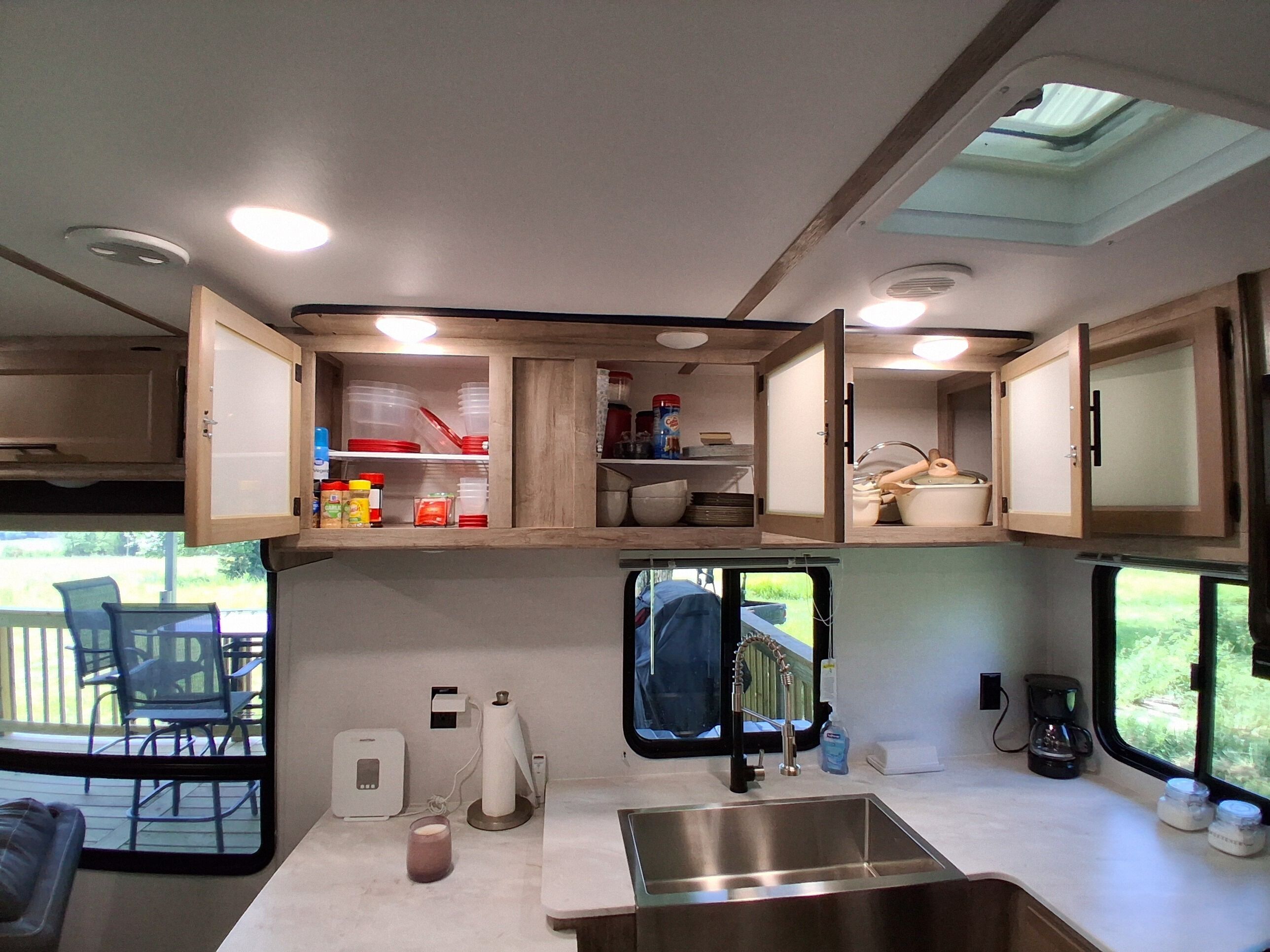Une cuisine compacte pour camping-car, équipée d’un évier, de placards de rangement et d’une fenêtre donnant sur une terrasse.