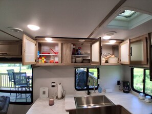 A compact RV kitchen with a sink, storage cabinets, and a window overlooking a deck.