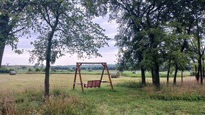 A wooden swing set in a grassy field with trees in the background.