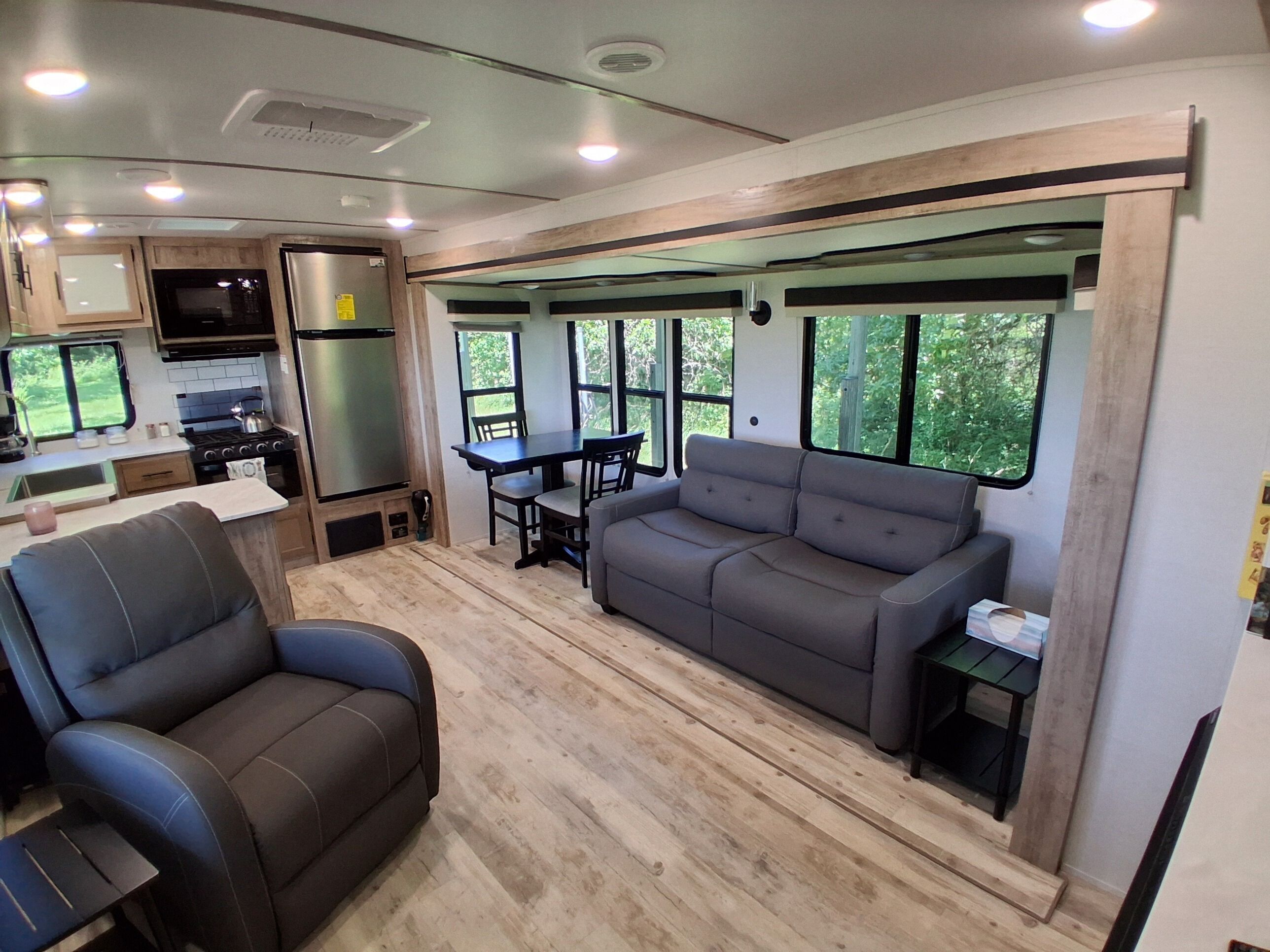 A compact RV interior with a kitchenette, a dining area, and seating.