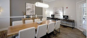 A conference room with a long wooden table, white upholstered chairs, and two desks with computers. - Landing | Chic 1BD, Gym, Pool (Orlando)