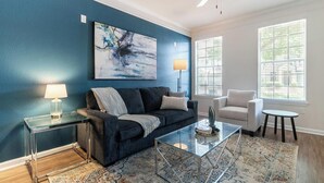 Una sala de estar con una pared azul oscuro, una mesa de centro de vidrio, un sofá, un sillón y una lámpara.