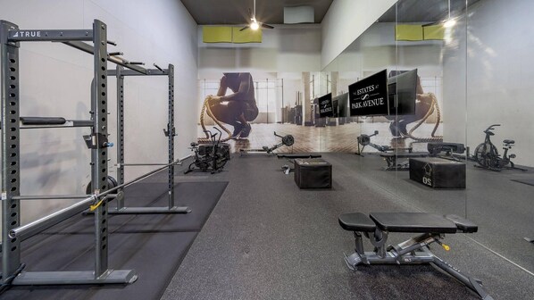 Une salle de sport équipée de matériel de musculation, de machines de cardio et dotée d’un grand miroir qui reflète l’espace.