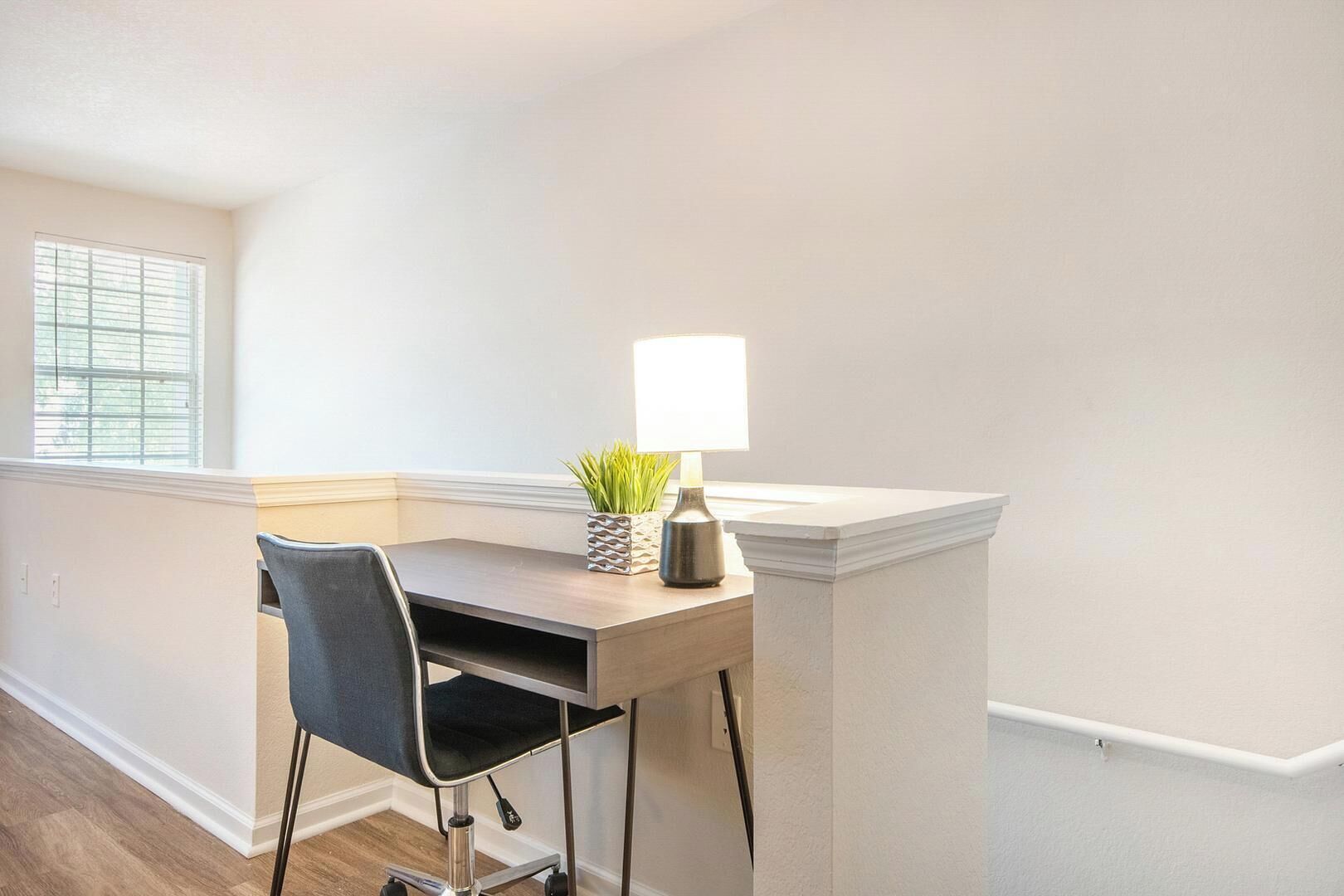 A corner office with a desk, chair, lamp, and a small plant.